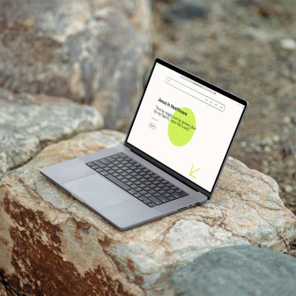 Jeusus In Healthcare homepage design on a laptop purched on a rock.